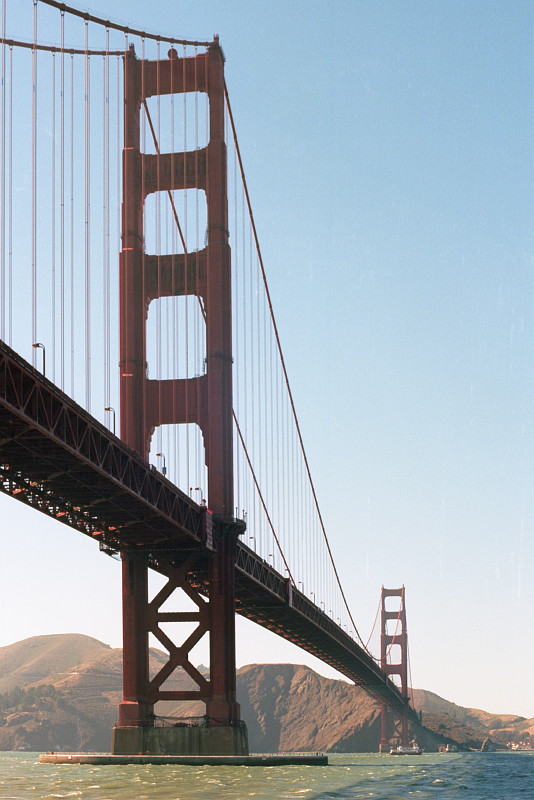 Golden Gate Bridge seen from sea level, the mountains of Marin Headlands visible in the distance. Out of sight to the left is Fort Point, guardian of the Golden Gate, dating back to the nineteenth century.