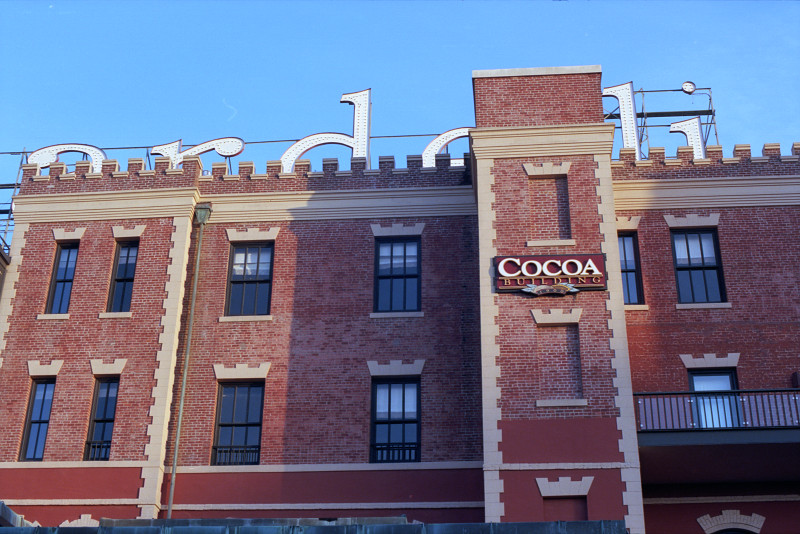 This three story red brick building at Ghirardelli Square, with sandstone lintels over the tall windows, has the delicious name 'Cocoa'. Above the building, the large white Ghirardelli sign and the blue sky completing the picture.