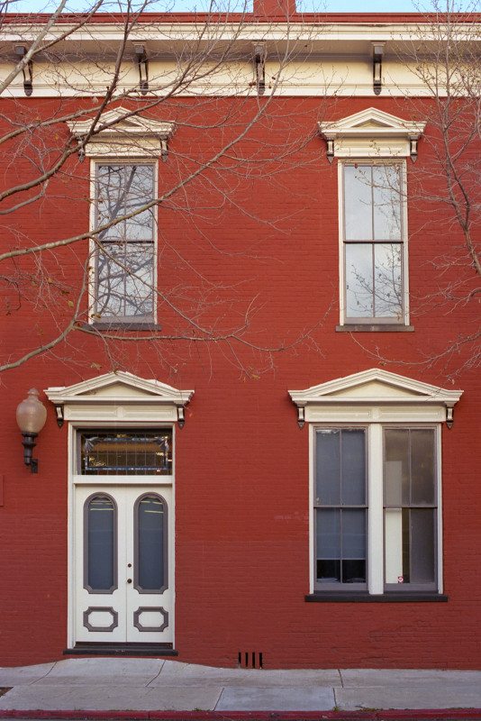 Red ochre brick building, showing the doorway to the sidewalk with a double-wide window next to the doorway. Building in Federalist period style. The Alameda, San José.