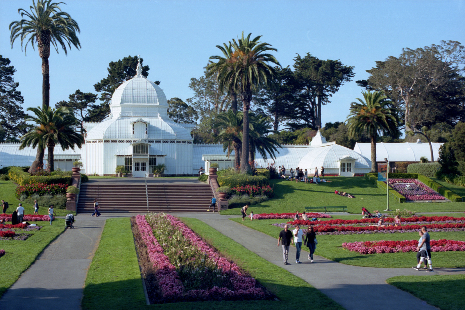 The Hall of Flowers in Golden Gate Park. The building has a central dome with wings extending left and right and perpendicular extensions at each end. It is all panes of glass, painted white, in a wooden framework.