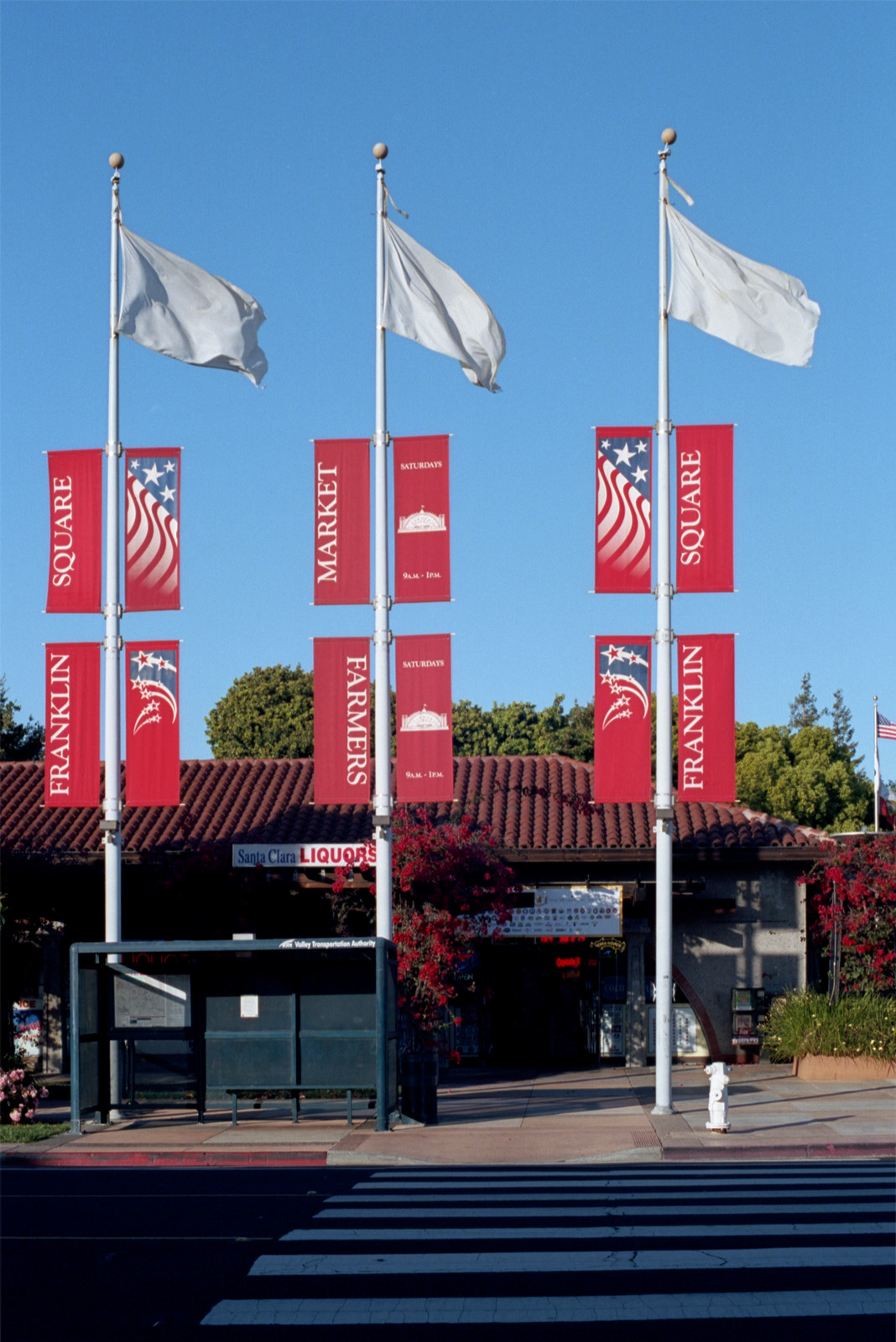 Three white flagpoles raise white flags and red scrolls announcing Franklin Plaza in Santa Clara, the center of the municipality. There are a number of businesses here in this pleasant environment.